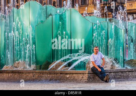 Ein junger Mann sitzt am modernen Brunnen im Breslauer Altstädter Markt oder Rynek. Stockfoto