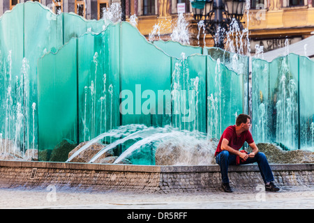 Ein junger Mann sitzt am modernen Brunnen im Breslauer Altstädter Markt oder Rynek. Stockfoto