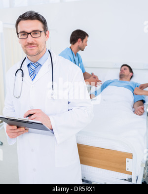 Arzt hält Berichte mit Patient und Chirurg im Hintergrund Stockfoto