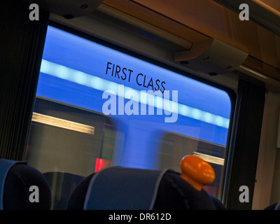 First Class-Schild am Fenster von Eisenbahnwagen mit unscharfen vorbeifahrenden Zug hinter UK Stockfoto