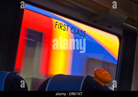 First Class-Schild am Fenster von Eisenbahnwagen mit unscharfen vorbeifahrenden Zug hinter UK Stockfoto