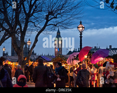 LONDON WEIHNACHTSMARKT SHOPPER LICHTER WESTMINSTER South Bank Weihnachtsmarkt Stände und Käufern mit Häusern des Parlaments hinter bei Dämmerung London UK Stockfoto