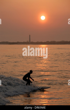 Mann, Surfen im Atlantik am Strand in Cape May, New Jersey bei Sonnenuntergang. Im Hintergrund ist der Cape kann Leuchtturm. Stockfoto