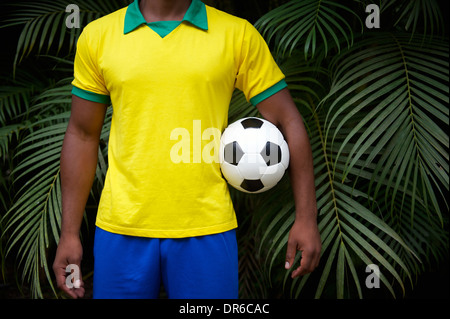 Brasilianischer Fußballspieler in Brasilien Farben uniform stehen in tropischer Palmen Dschungel mit Soccer ball Stockfoto