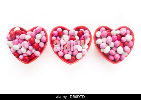 Drei Herz-geformte Schüsseln voll Candy-beschichtete Pralinen isoliert auf weiss Stockfoto