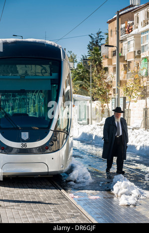 Jerusalem, Israel. Ein Ultra-orthodoxer jüdischer Mann geht eine nicht-operative Stadtbahn, im Schnee stecken. Stockfoto