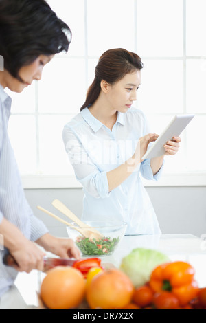 eine Frau, die Schneiden von Gemüse, während die andere Frau Tablet PC verwendet Stockfoto