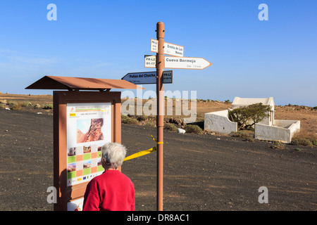 Ältere Frau liest touristische Informationen Zeichen zeigt Wanderwege an Famara Aussichtspunkt. Haria Lanzarote Kanarische Inseln Spanien Stockfoto