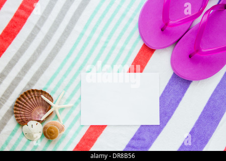 Strand-Szene mit lila Flip-Flops, Muscheln, Seesterne und einen Sand Dollar auf einem gestreiften Strandtuch mit Textfreiraum. Stockfoto