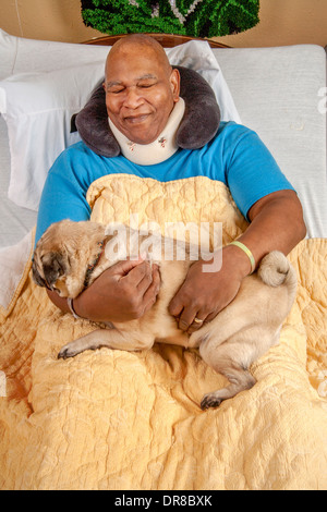 Eine afroamerikanische Krankenhauspatient in Südkalifornien schmiegt sich ein Mops Komfort von einem freiwilligen gebracht. MODEL-RELEASE Stockfoto