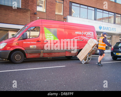 Parcel Force Lieferung van mit Auslieferungsfahrer ziehen gestapelt Pakete über eine Straße mit einem Handtruck-Feld-Träger Stockfoto