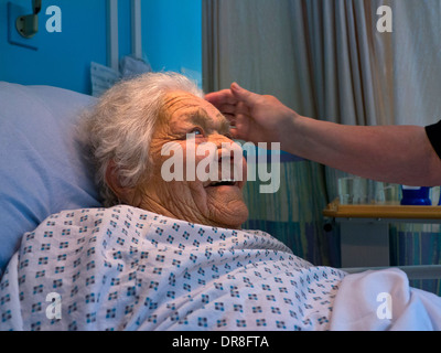 Ältere lachende Krankenschwester im Krankenhaus zufrieden lächelnd ältere Dame im Krankenhausbett mit tröstender Hand der Krankenschwester Stockfoto