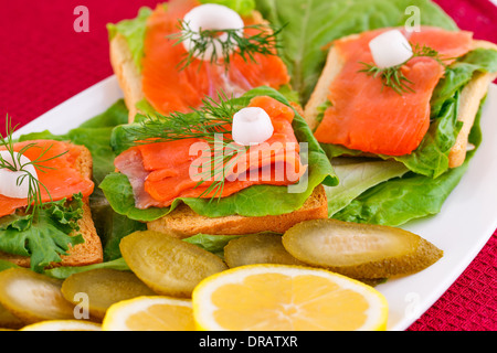 Lachs Sandwiches mit Salat, frische und eingelegte Gurken, Zwiebel, Zitrone auf Platte. Stockfoto