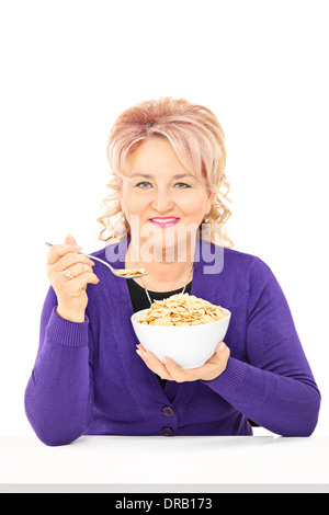 Reife Dame essen Müsli aus einer Schüssel auf dem Tisch sitzend Stockfoto