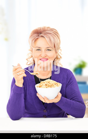 Reife Frau essen Getreide in einer Schüssel auf dem Tisch zu Hause Stockfoto