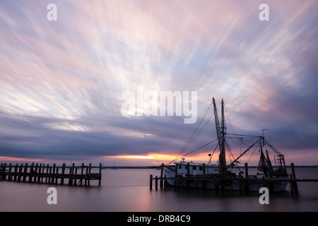 Lange Exposition Sonnenuntergang mit Wolken über ein Garnelen-Boot von Schlieren gefesselt an ein altes Dock in Fernandina Beach, Florida. Stockfoto