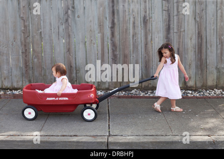 Ältere Schwester ihrer jüngeren Schwester in einem roten Wagen ziehen. Stockfoto