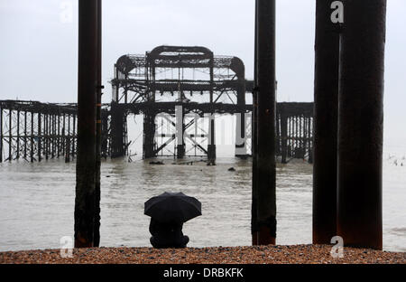 Eine Person sitzt unter einem Regenschirm Ausblick auf das Meer von der West Pier in Brighton Beach im Nieselregen und frühen Morgennebel UK Stockfoto