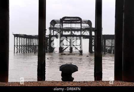 Eine Person sitzt unter einem Regenschirm Ausblick auf das Meer von der West Pier in Brighton Beach im Nieselregen und frühen Morgennebel UK Stockfoto