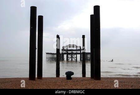 Eine Person sitzt unter einem Regenschirm Ausblick auf das Meer von der West Pier in Brighton Beach im Nieselregen und frühen Morgennebel UK Stockfoto