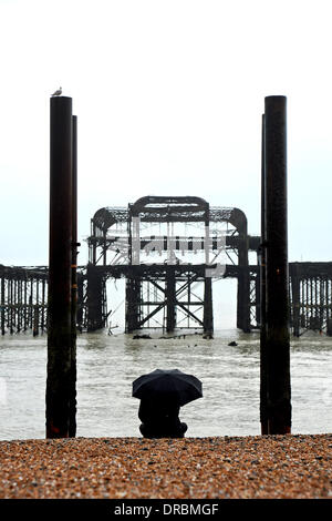 Eine Person sitzt unter einem Regenschirm Ausblick auf das Meer von der West Pier in Brighton Beach im Nieselregen und frühen Morgennebel UK Stockfoto