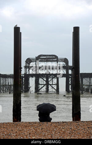 Eine Person sitzt unter einem Regenschirm Ausblick auf das Meer von der West Pier in Brighton Beach im Nieselregen und frühen Morgennebel UK Stockfoto