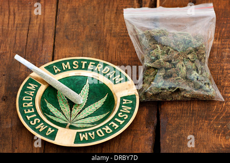 Marihuana-Joint in einem Aschenbecher mit Amsterdam Zeichen und eine große Plastiktüte des Unkrauts auf hölzernen Hintergrund Stockfoto