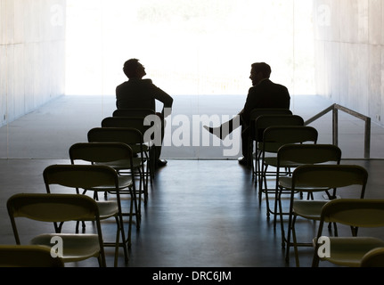 Geschäftsleute, die auf Stühlen in einer Reihe im Gespräch Stockfoto