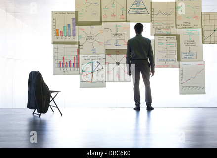 Geschäftsmann, Blick auf Grafiken und Diagramme auf Glaswand im Büro Stockfoto