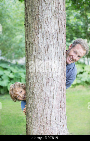 Vater und Sohn peering hinter Baum Stockfoto