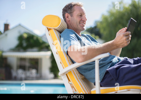 Mann liest im Liegestuhl am Pool Stockfoto