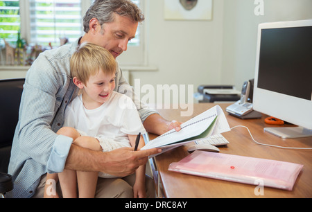 Sohn auf arbeitenden Vaters Schoß Stockfoto