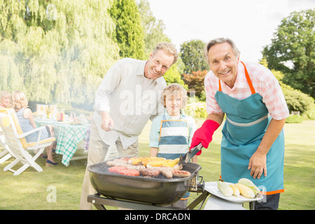 Generationsübergreifende Männer grillen Fleisch und Mais am Grill im Garten Stockfoto