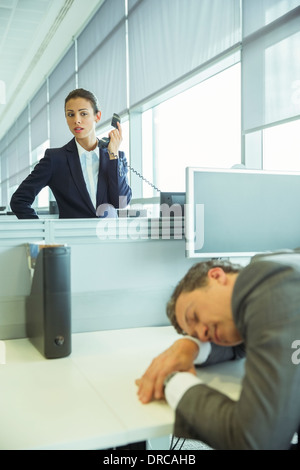 Geschäftsfrau beobachten schlafenden Geschäftsmann im Büro Stockfoto