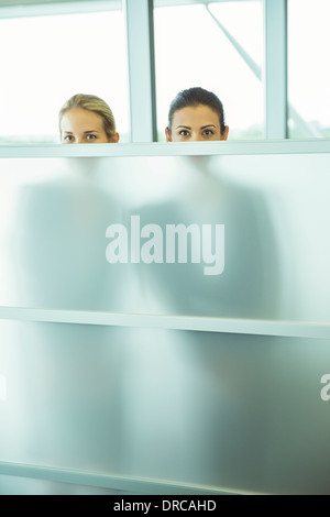 Geschäftsfrauen spähen über eine halbe Wand im Büro Stockfoto