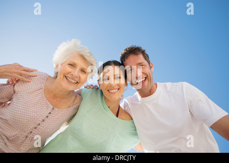 Ältere Frau umarmt paar gegen blauen Himmel Stockfoto