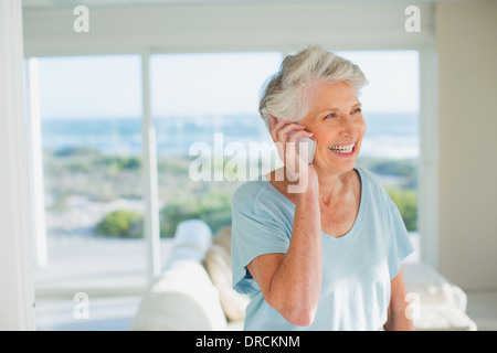 Ältere Frau am Handy im sonnigen Wohnzimmer Stockfoto