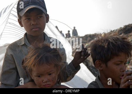 Drei junge Kinder-Arbeiter sind sich vor der heißen Sonne auf der giftigen Stung Meanchey Deponie in Phnom Penh, Kambodscha Schattierung. Stockfoto