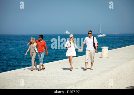 Junge Menschen, die zu Fuß über die Promenade, Boote im Hintergrund, Zadar, Kroatien Stockfoto