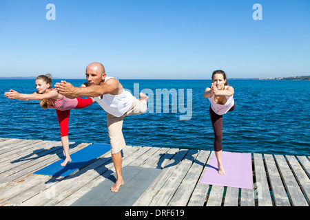 Menschen praktizieren Yoga auf einem Holzsteg, Krieger darstellen, auf einem Bein Stockfoto