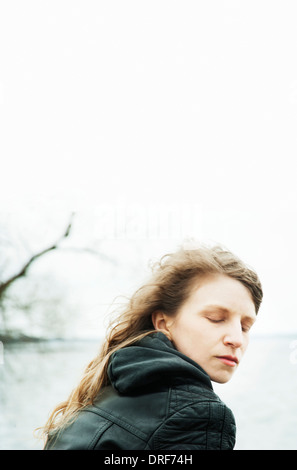 Junge Frau mit Augen geschlossen, langen blonden Haaren draußen sitzen auf windigen Tag Stockfoto