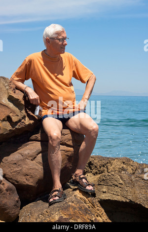 Porträt von senior Tourist Mann sitzt auf den felsigen Strand. Stockfoto
