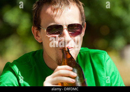 Nahaufnahme eines Jünglings glücklich trinken Bier aus der Flasche im Freien. Stockfoto