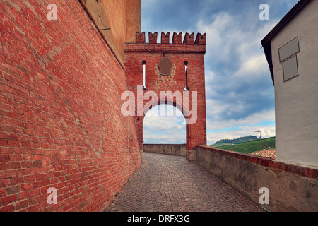 Schmalen gepflasterten Straße entlang der roten Backsteinmauer und Fragment eines mittelalterlichen gewölbten Durchgang in Barolo, Italien. Stockfoto