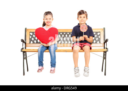 Zwei Kinder sitzen auf Bank mit großen roten Herz und einen Lolli Stockfoto