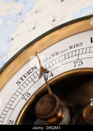 Nahaufnahme einer Vintage aneroid Baromter (ab den 1930er) vor eine Wetterkarte. Baromter zeigt wechselhaftes Wetter Stockfoto