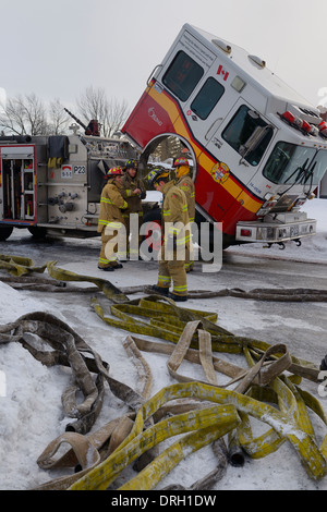 Feuerwehrleute ein Pumper Löschfahrzeug im Winter verworrenen Schläuche aufräumen, nachdem ein Haus Feuer in Ottawa Kanada Stockfoto