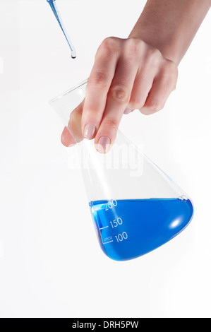 Ein Wissenschaftler Tropfen einer Lösung aus einer Pipette in einem konischen Kolben mit einer blauen Lösung hinzufügen Stockfoto