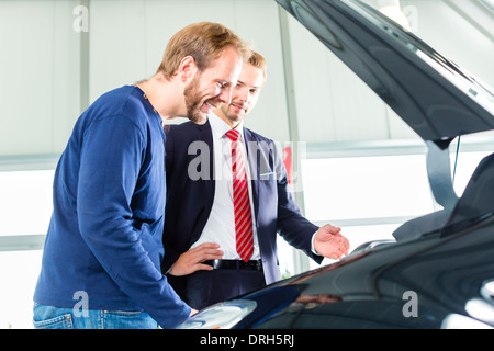 Verkäufer oder Auto Verkäufer und Klienten oder Kunden im Autohaus präsentieren die Motorleistung von neu- und Gebrauchtwagen Stockfoto