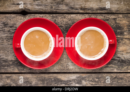 Zwei rote Tassen von Kaffee mit Milch auf alten Holz-Hintergrund. Ansicht von oben Stockfoto